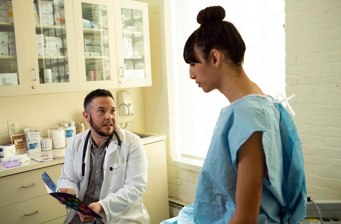 A transgender woman in a hospital gown speak ... ctor, a transgender man, in an exam room